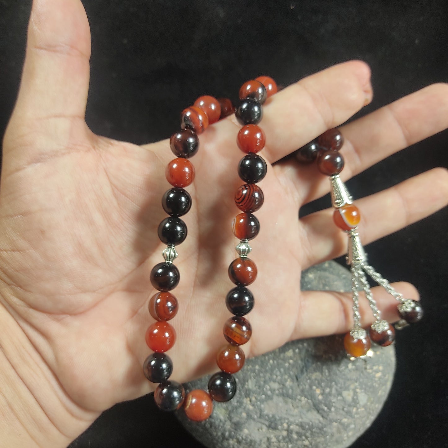 Hand holding a bracelet with red and black beads on a dark background